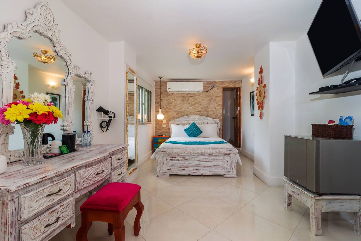 A bedroom with a bed, dresser, TV, and a mirror.