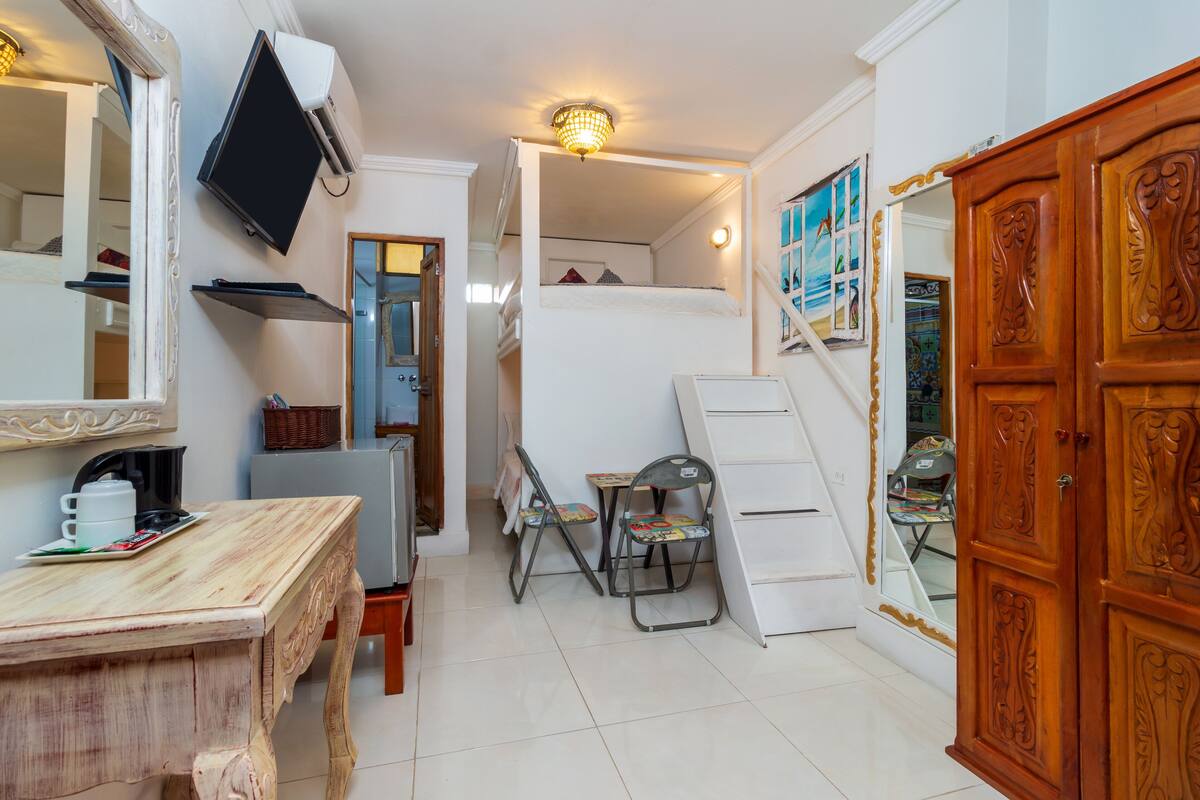 A compact room with a bunk bed, a desk with a chair, a television, and a wardrobe.