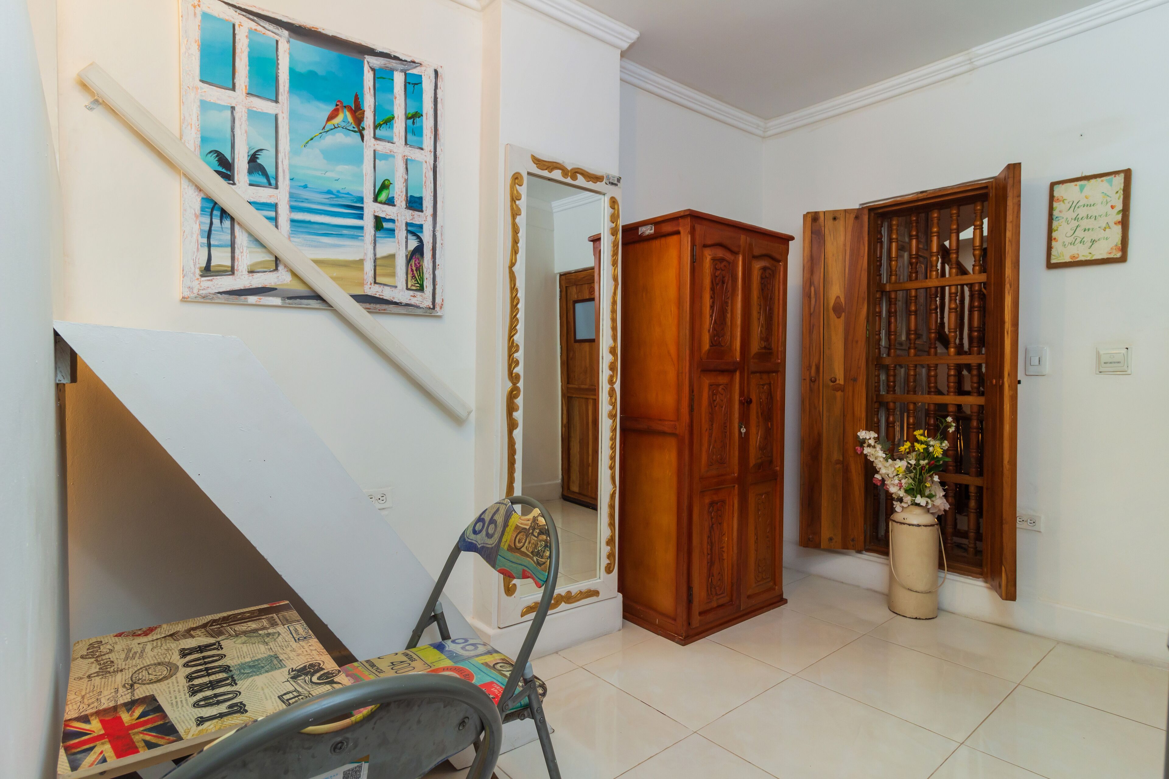 A room with a wooden cabinet, a mirror, a window with a beach scene, and a chair with a map design.