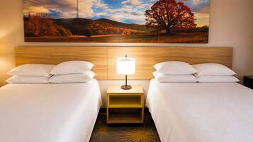 Een hotelkamer met twee bedden, een nachtkastje met een lamp, en een groot landschap op de muur.