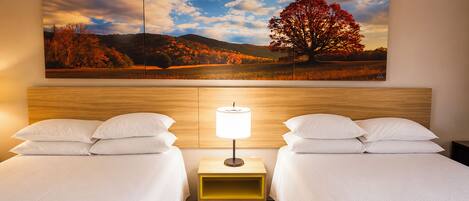 A hotel room with two beds, a nightstand with a lamp, and a large landscape painting on the wall.