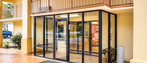 A hotel entrance with a glass door, a balcony, and a car parked outside.