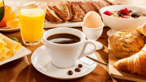 A breakfast setting with a cup of coffee, orange juice, bread, pastries, and a bowl of cereal with fruits. - Hotel Brewton (Brewton)