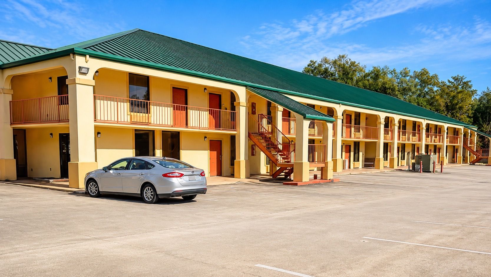 Un motel con varios balcones, una zona de estacionamiento techada y una escalera que lleva a los pisos superiores.