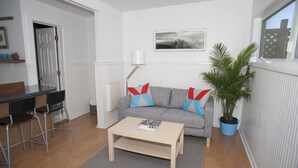 A living room with a grey sofa, a wooden coffee table, a lamp, a potted plant, and a dining area with a table and chairs.