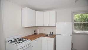 A kitchen with white cabinets, a wooden countertop, a gas stove, a sink, and a refrigerator.