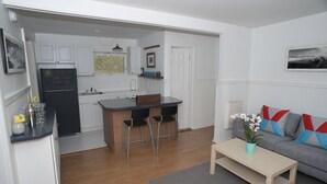 A modern kitchen with white cabinets, a black refrigerator, and a bar area with two chairs.