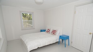 A white bedroom with a bed, a nightstand, a window, and a door.