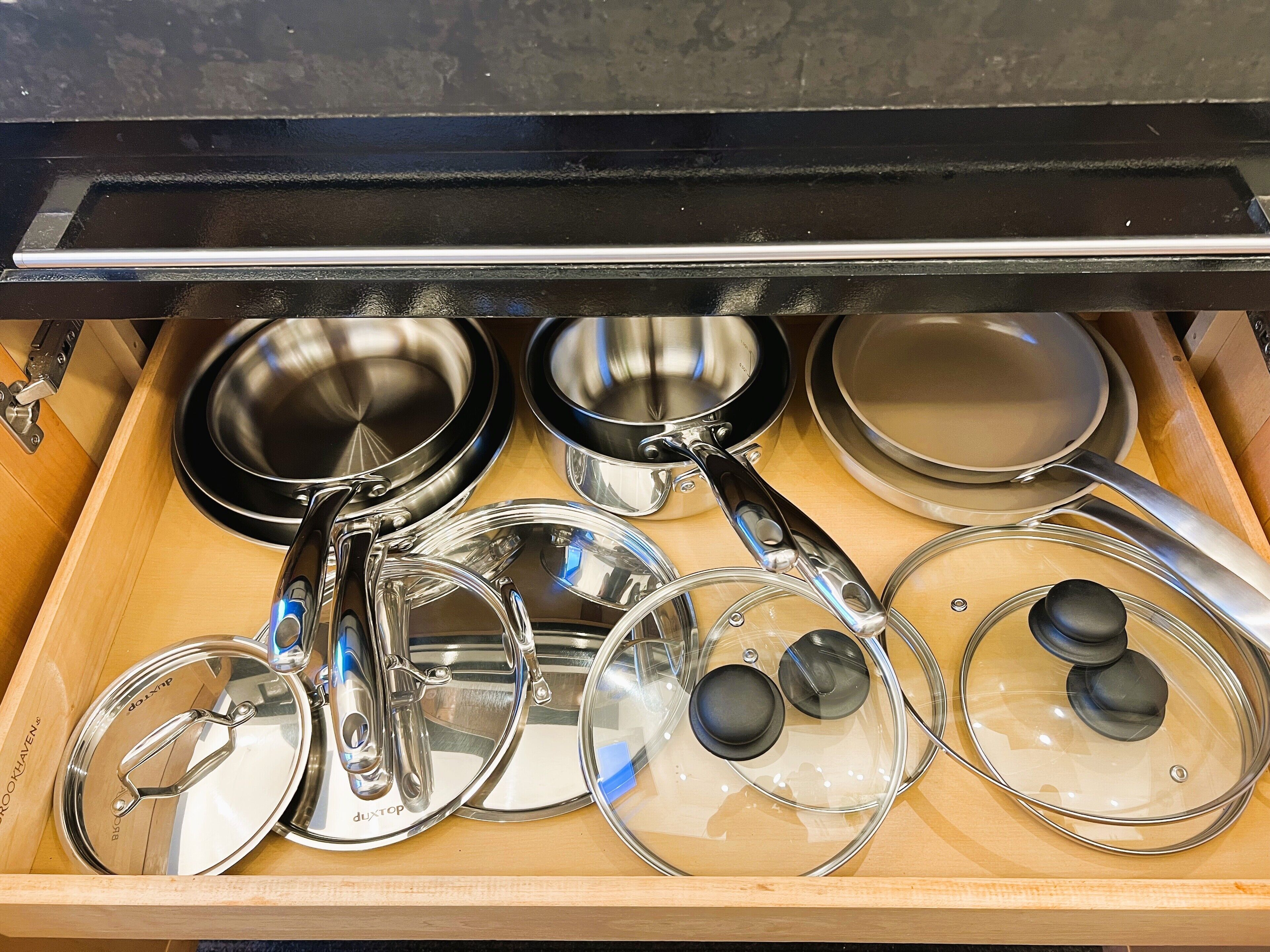 A drawer containing various kitchen utensils including pots, pans, and lids.