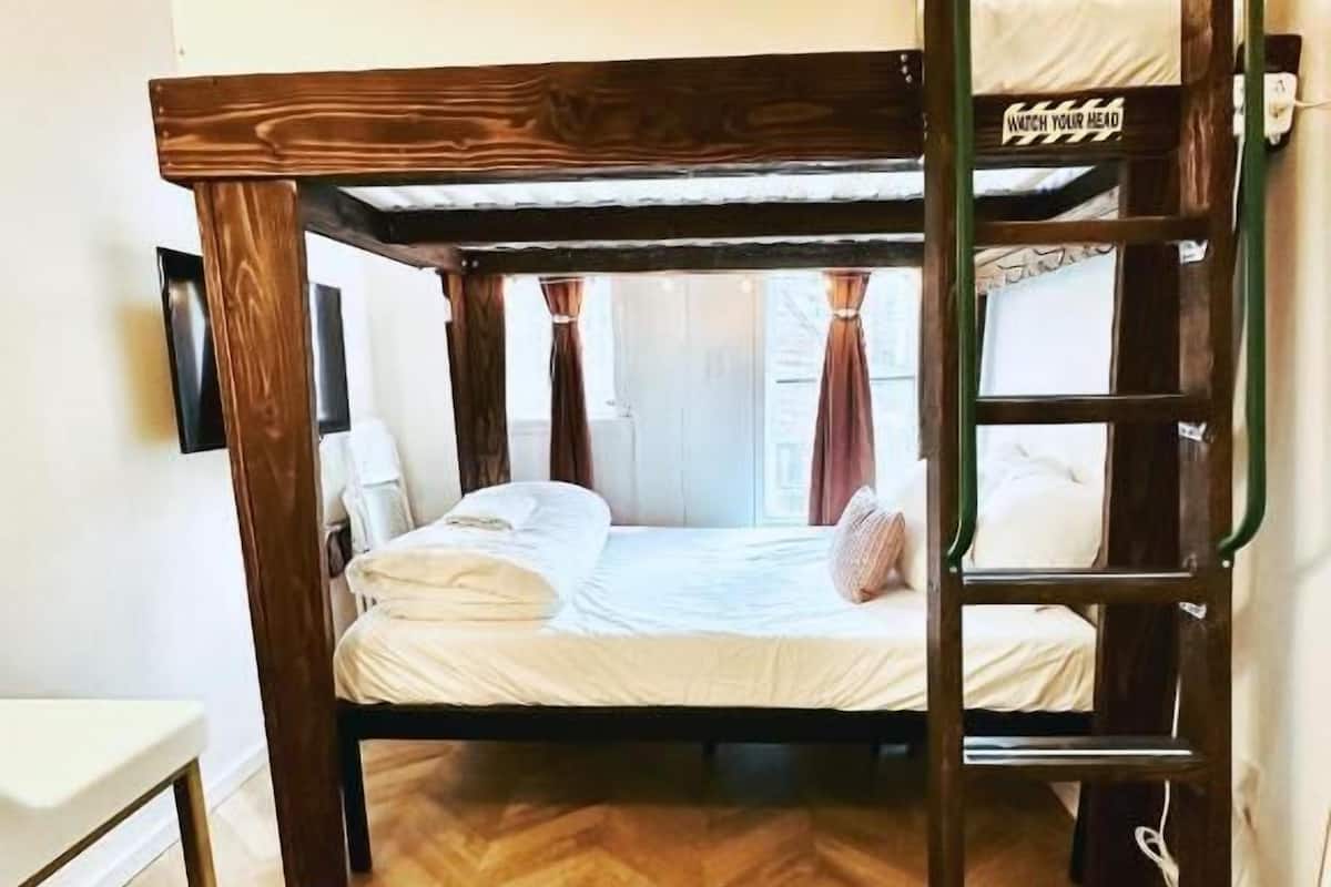 Ein Schlafzimmer mit Etagenbetten, einer Holzleiter, einem kleinen Tisch mit einem Glas und Blick ins Freie durch das Fenster.