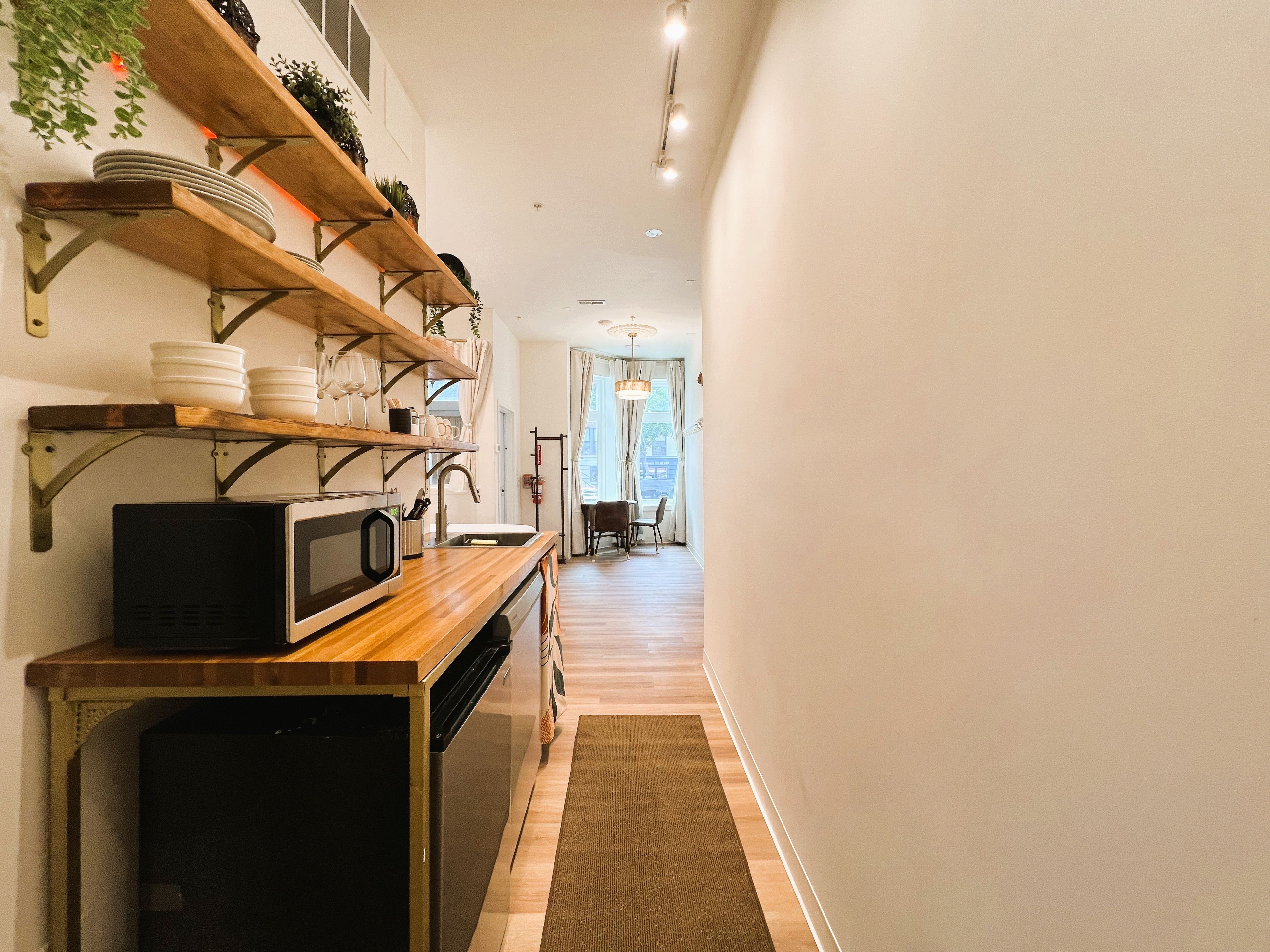 Una cocina con microondas, estantes con vajilla y vistas a un comedor.
