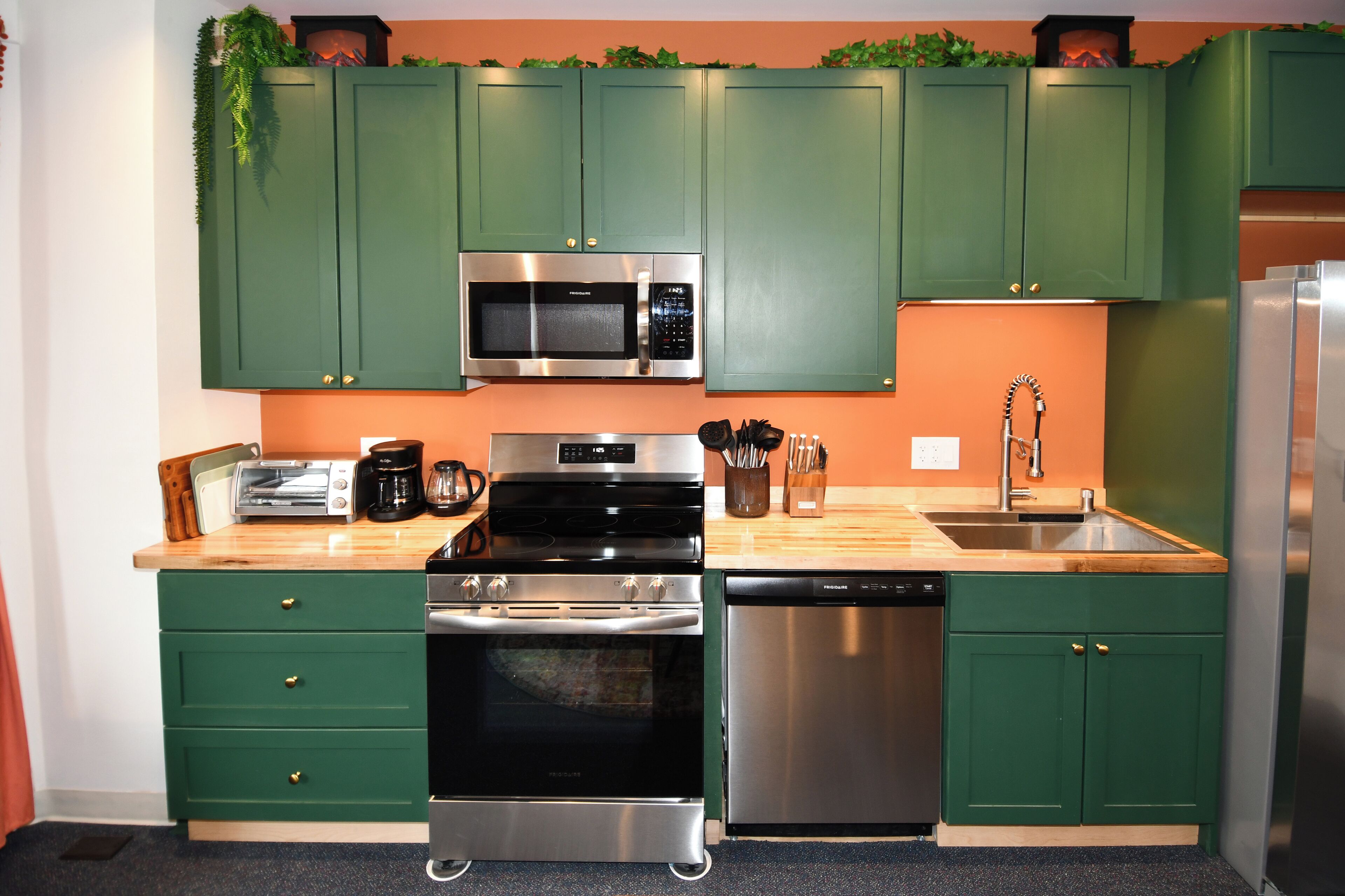 A kitchen with green cabinets, a microwave, stove, oven, dishwasher, and a sink.