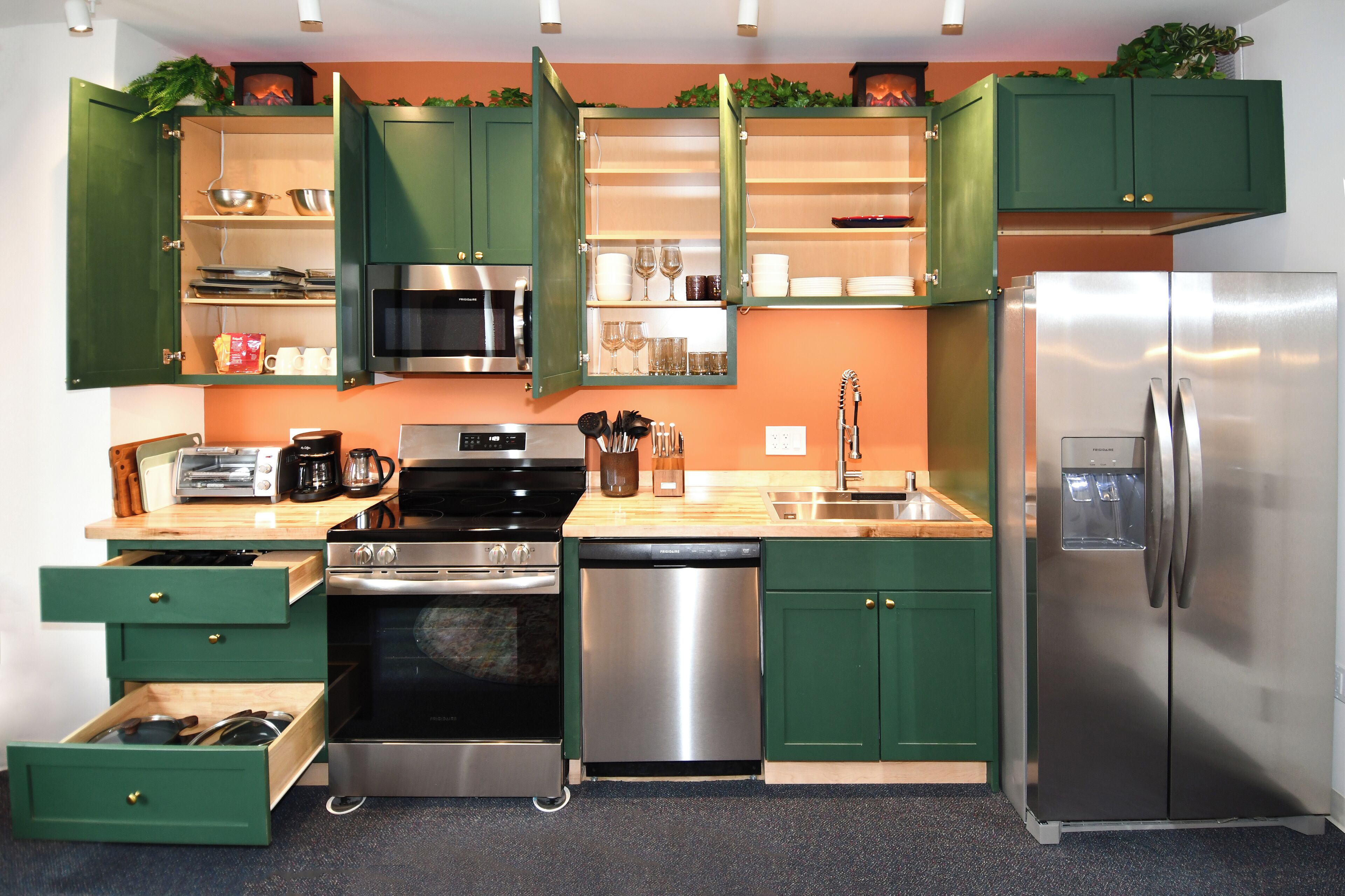 A kitchen with green cabinets, stainless steel appliances, and a wooden countertop.