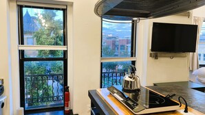A kitchen with a modern induction cooktop, a kettle, and a fire extinguisher. There are two windows with views of a balcony and buildings. - HighRoad Washington DC (Washington)