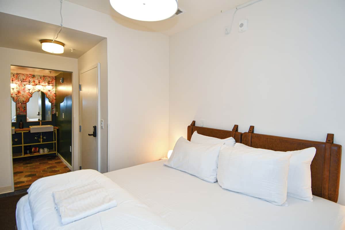 Ein Hotelzimmer mit einem großen Bett, einem Holzkopfstück und einem durchgegangenen Tür sichtbar liegenden Badezimmer.