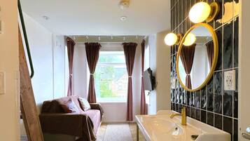 Un dormitorio con cama, ventana con cortinas, baño con lavabo y espejo, y vistas a zonas verdes.