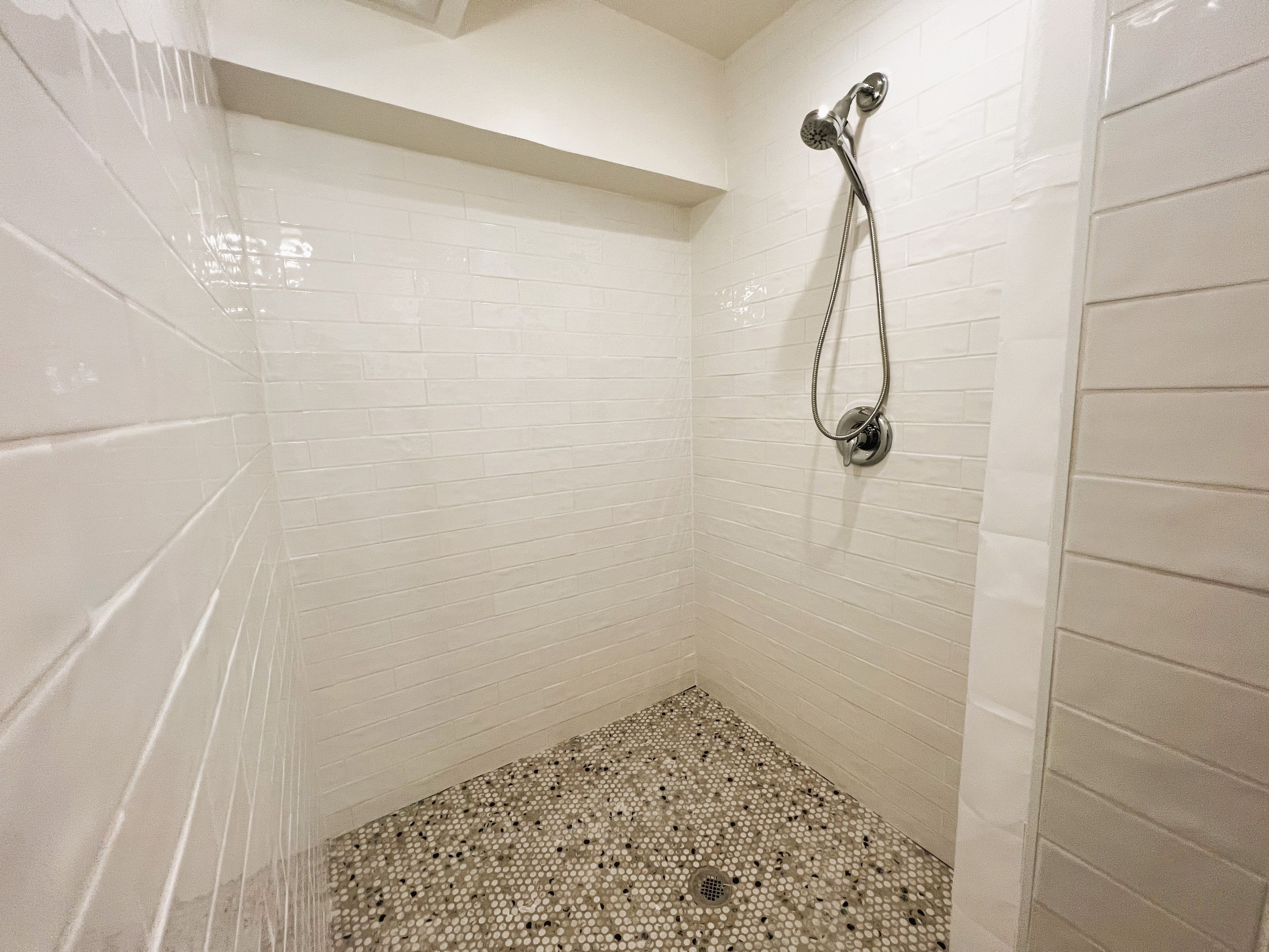 Una ducha con paredes de azulejos blancos y un suelo con diseño tipo mosaico.