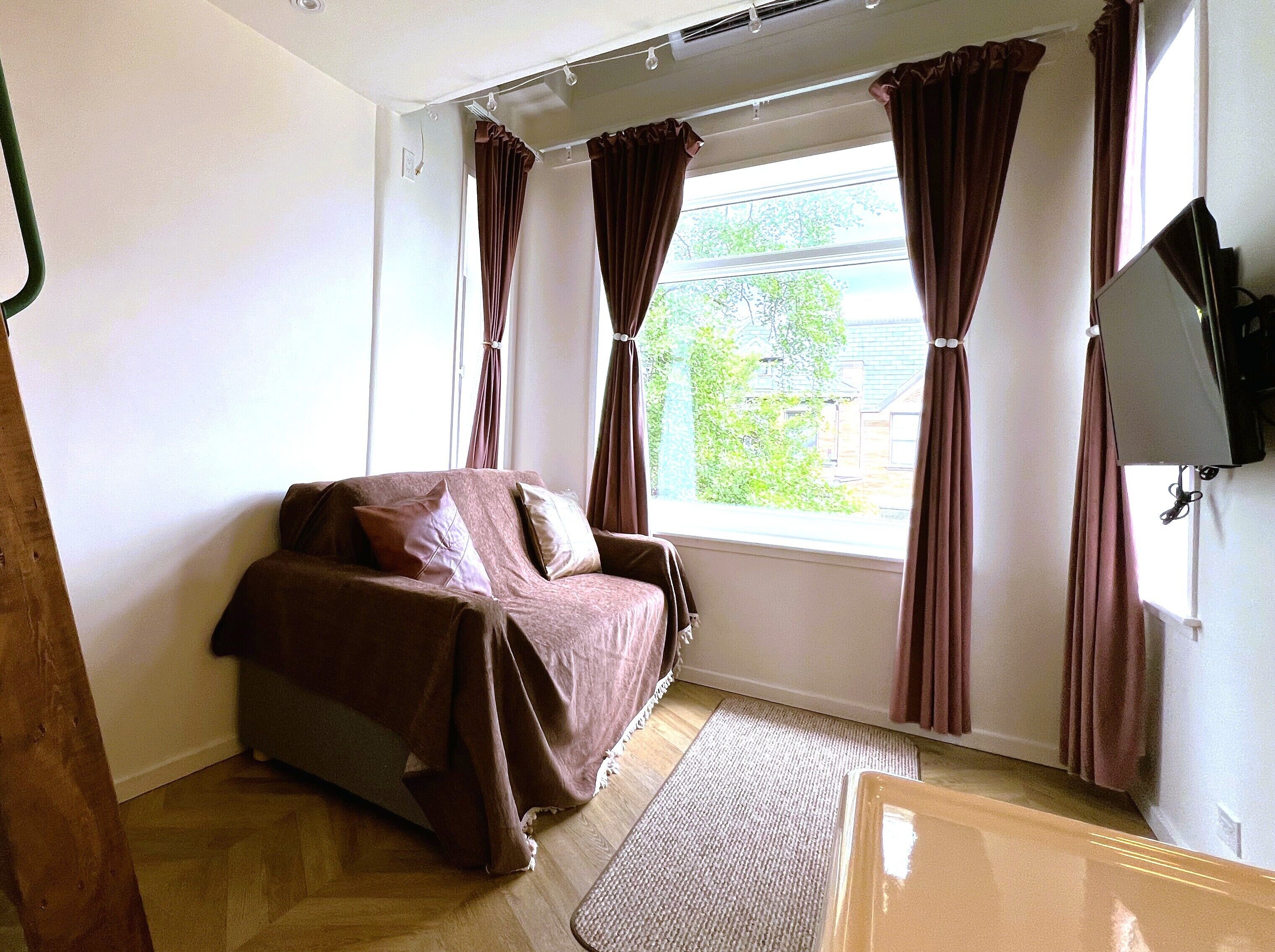Una habitació amb un llit, una finestra amb cortines, una televisió i un paviment de fusta.