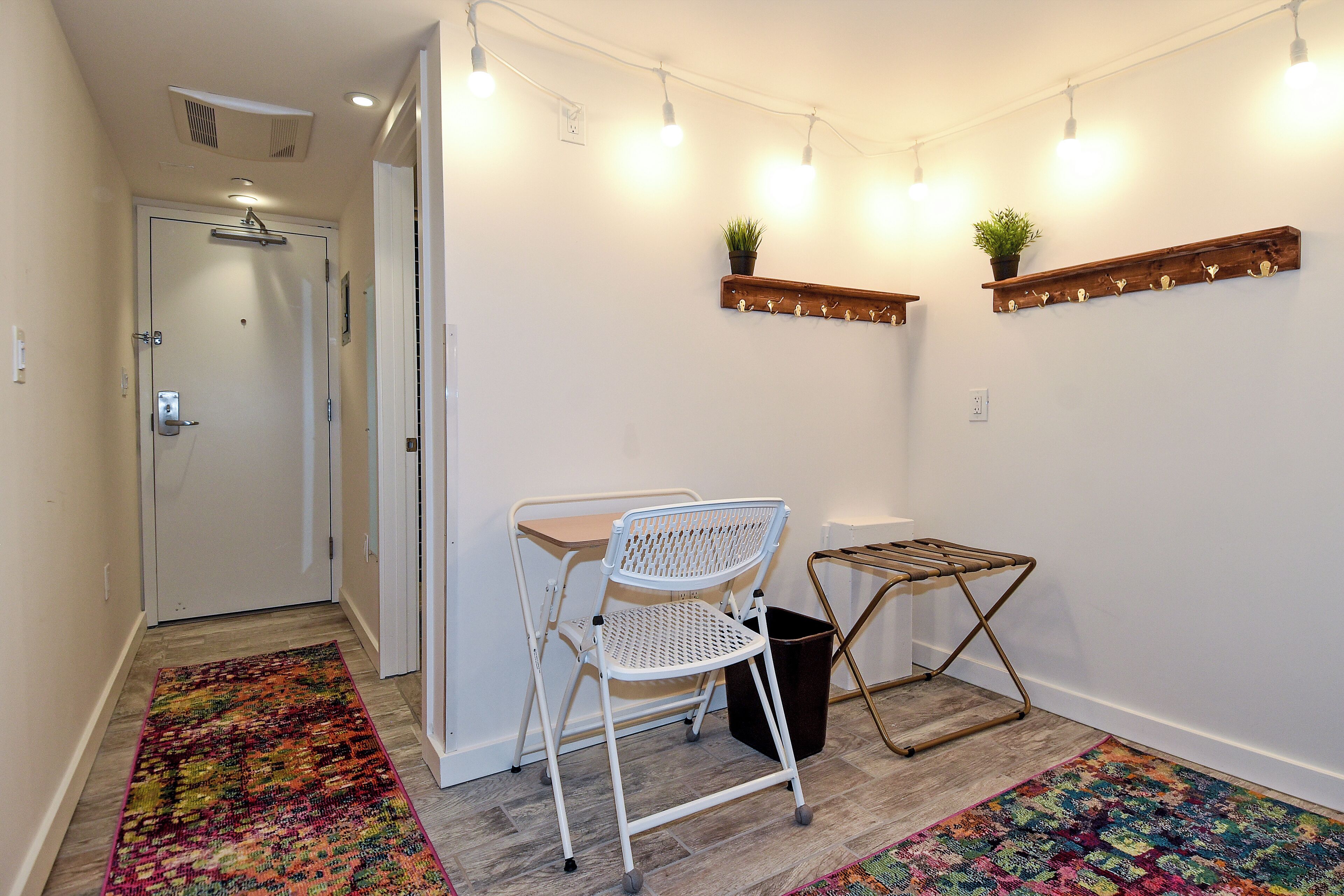 A hallway with a white folding chair, a small table, a trash bin, and a colorful rug.