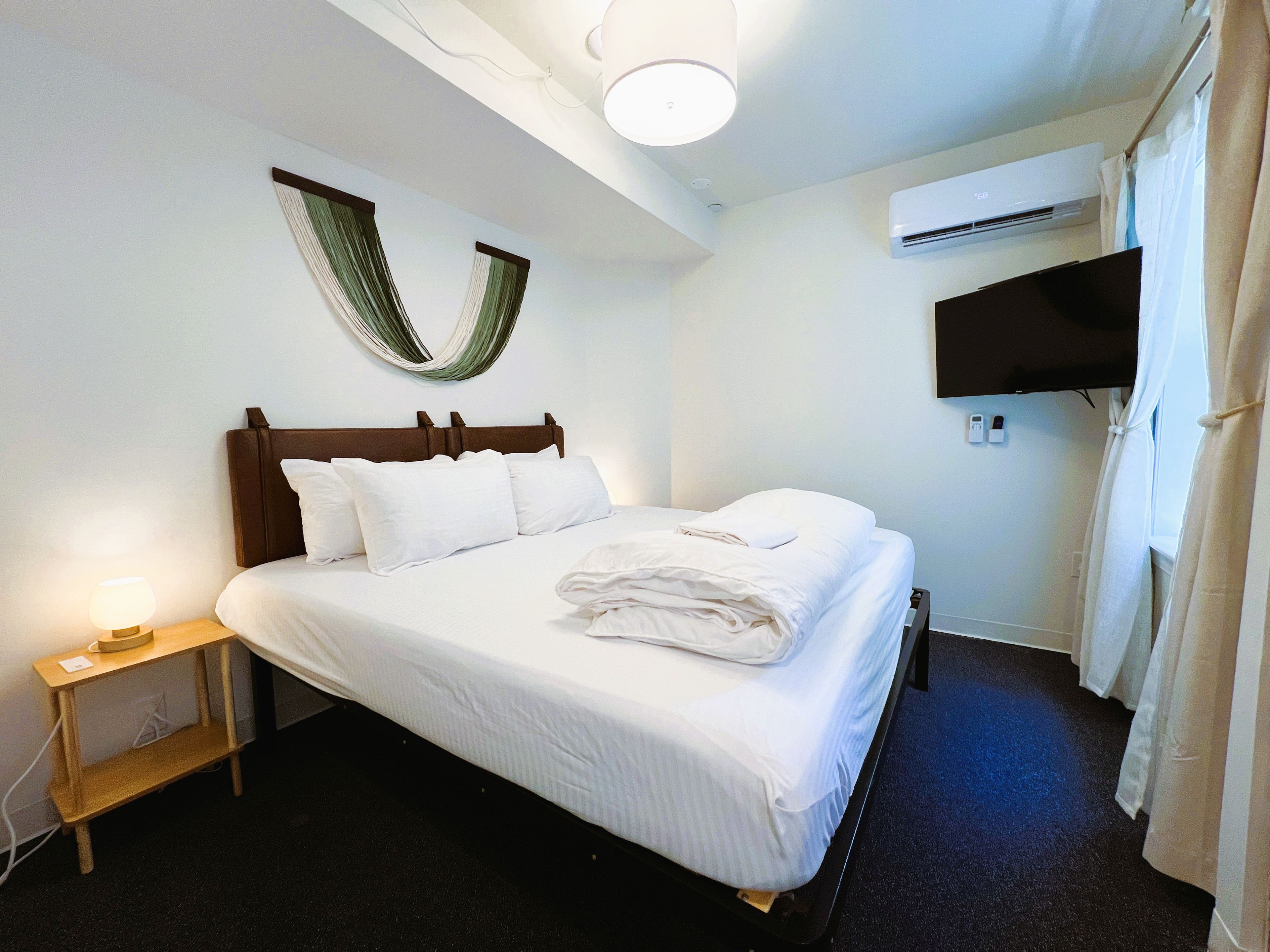 Habitación de hotel con cama, lámpara de noche, televisor montado en la pared y aire acondicionado.