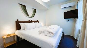 Habitación de hotel con cama, lámpara de noche, televisor montado en la pared y aire acondicionado.