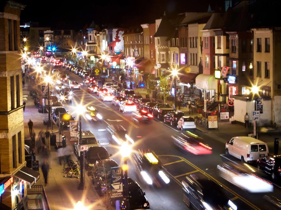 A busy urban street at night with multiple lanes of traffic and illuminated storefronts.