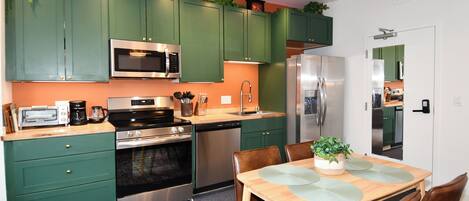 A modern kitchen with green cabinets, stainless steel appliances, and a wooden dining table with chairs.
