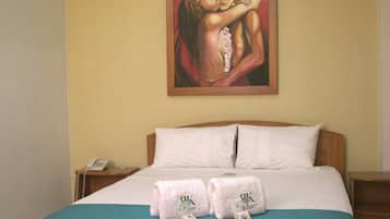 A hotel room with a wooden bed, a painting on the wall, and an air conditioner above the bed.