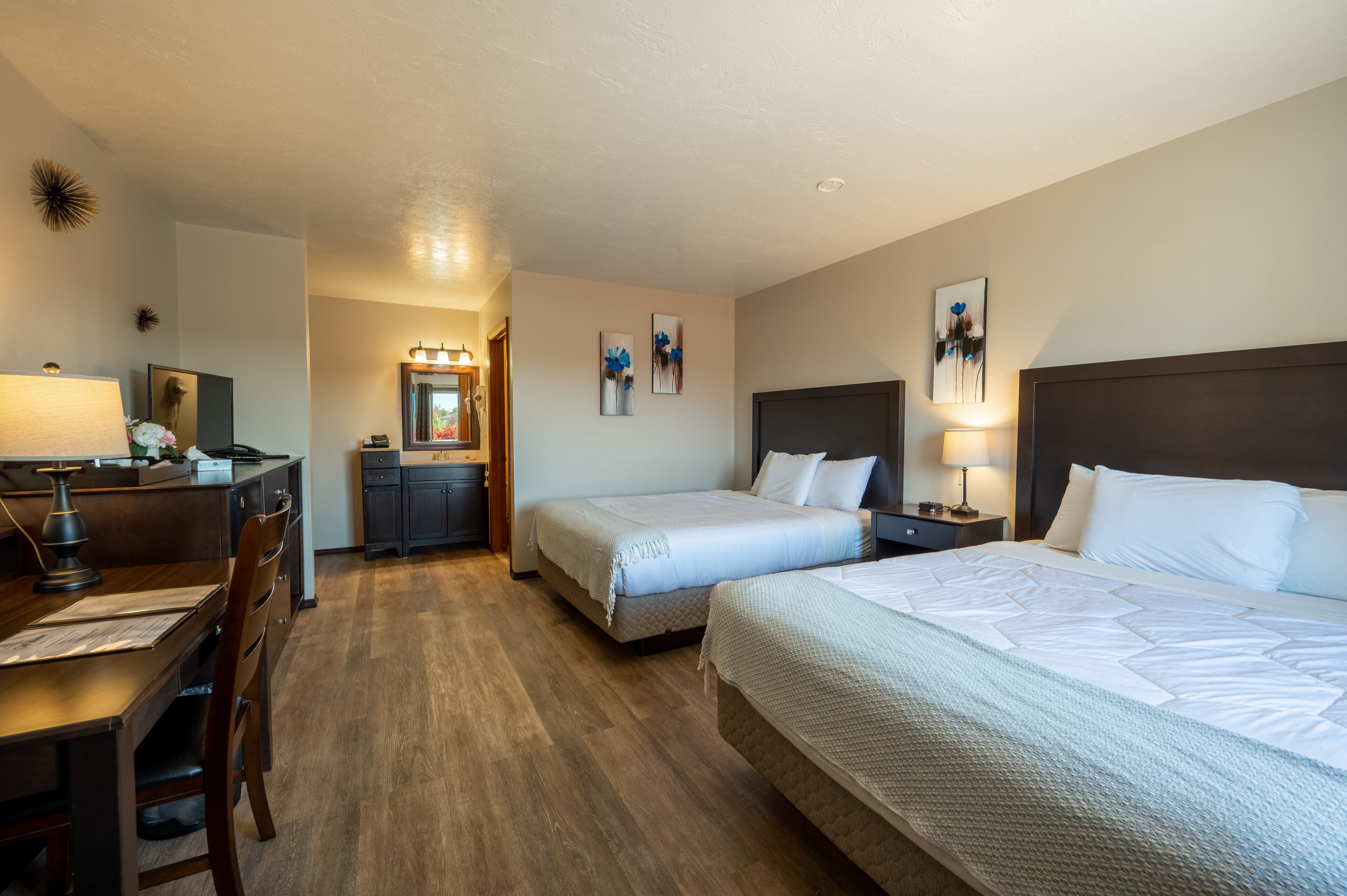 A hotel room with two beds, a desk, a chair, a dresser, and a mirror.