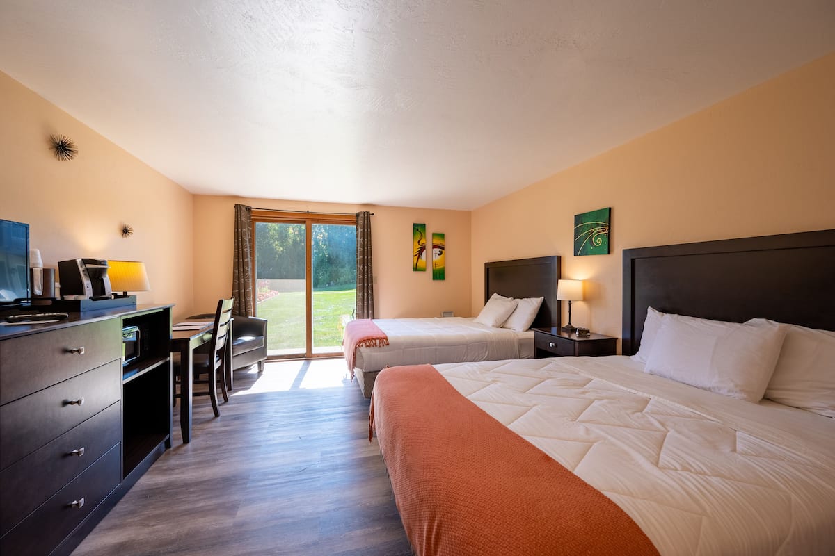 A hotel room with two beds, a desk with a computer, a chair, and a view of a garden through the window.