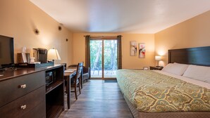 A hotel room with a bed, a desk, a chair, a TV, and a window with a view of trees. - Sister Bay Inn (Sister Bay)