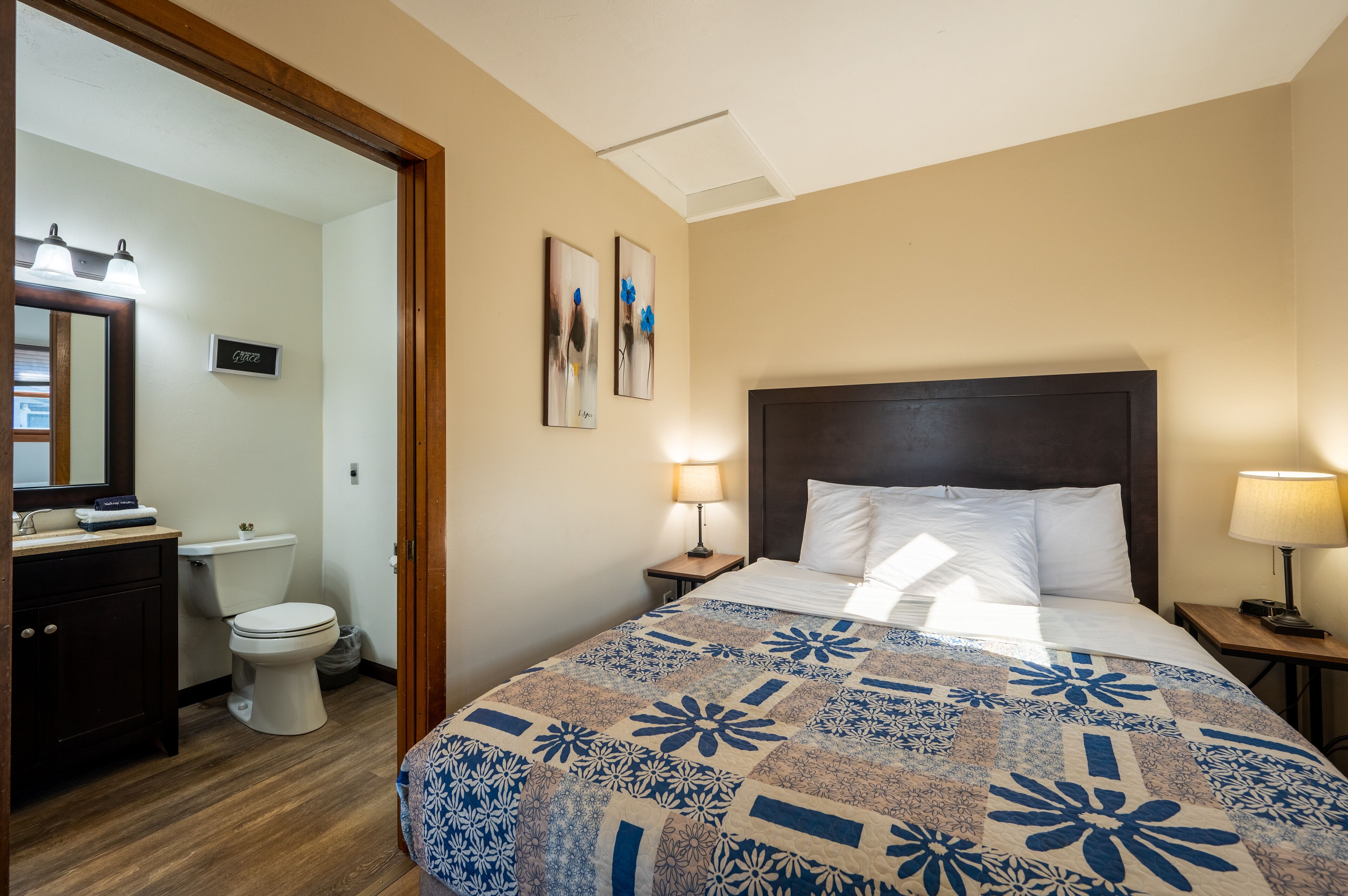 Ein Hotelzimmer mit Bett, Nachttisch mit Lampe, Badezimmer mit Toilette und Waschbecken sowie Spiegel.