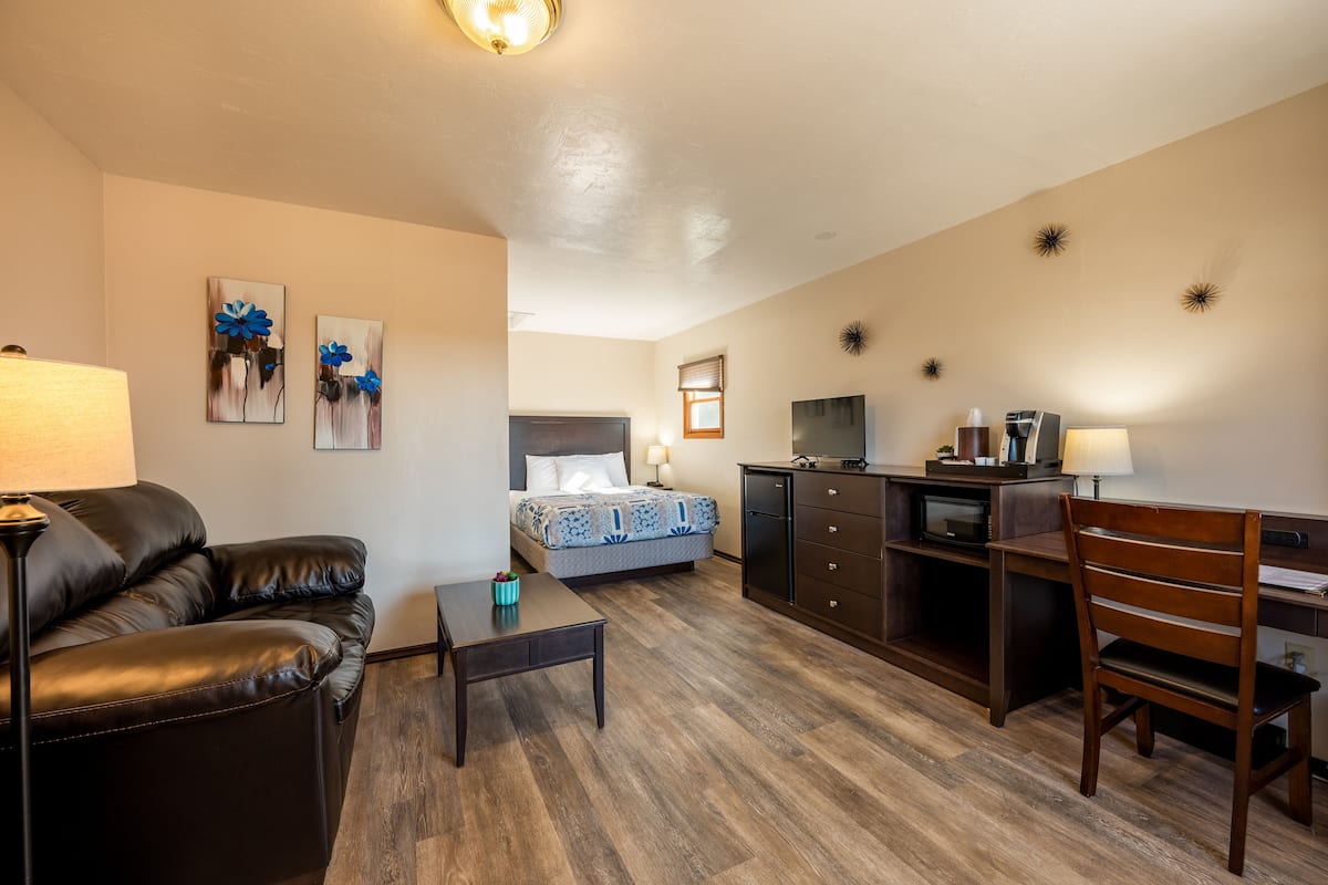A hotel room with a bed, a desk, a chair, a coffee machine, and a TV.