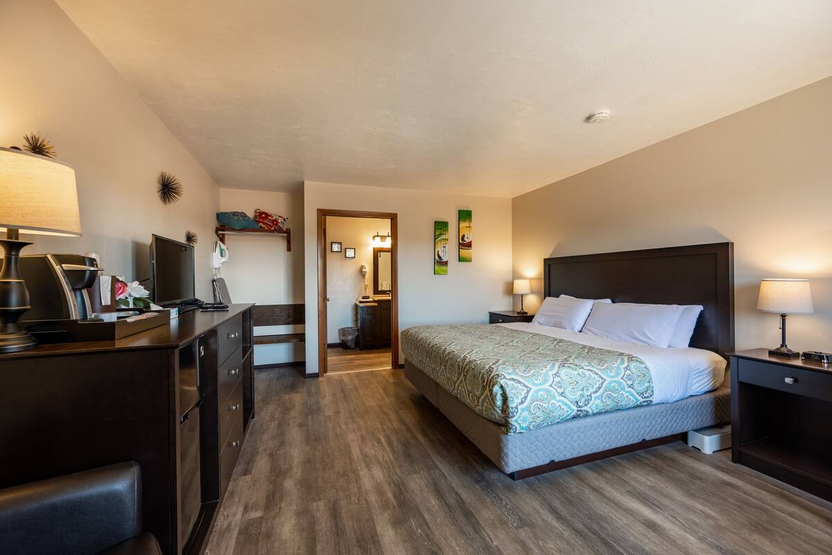 A hotel room with a bed, desk, and chair. There is a door leading to a bathroom and a hallway.