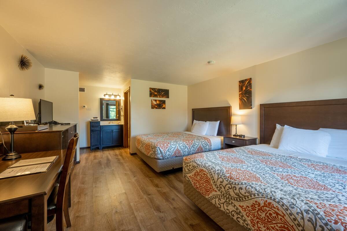 A hotel room with two beds, a desk with a lamp, a dresser, and a mirror.