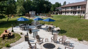 An outdoor patio with Adirondack chairs, a fire pit, and two blue umbrellas. - Sister Bay Inn (Sister Bay)