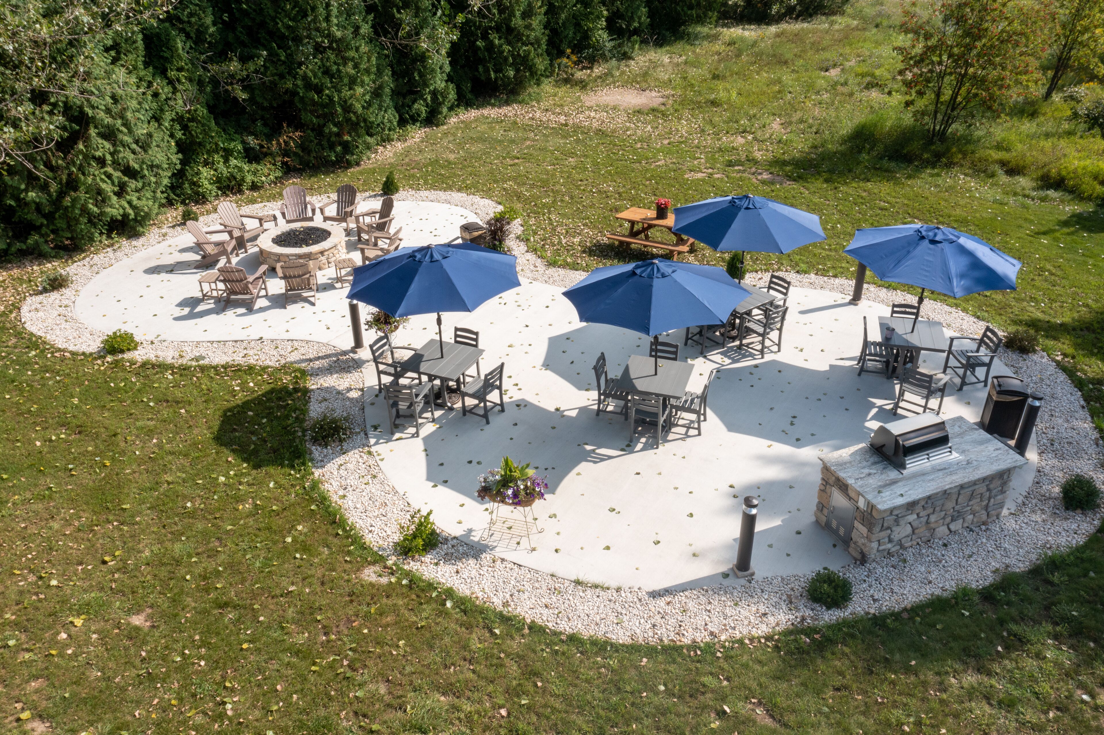 An outdoor patio area with round tables and chairs, surrounded by blue umbrellas, and a stone fireplace.