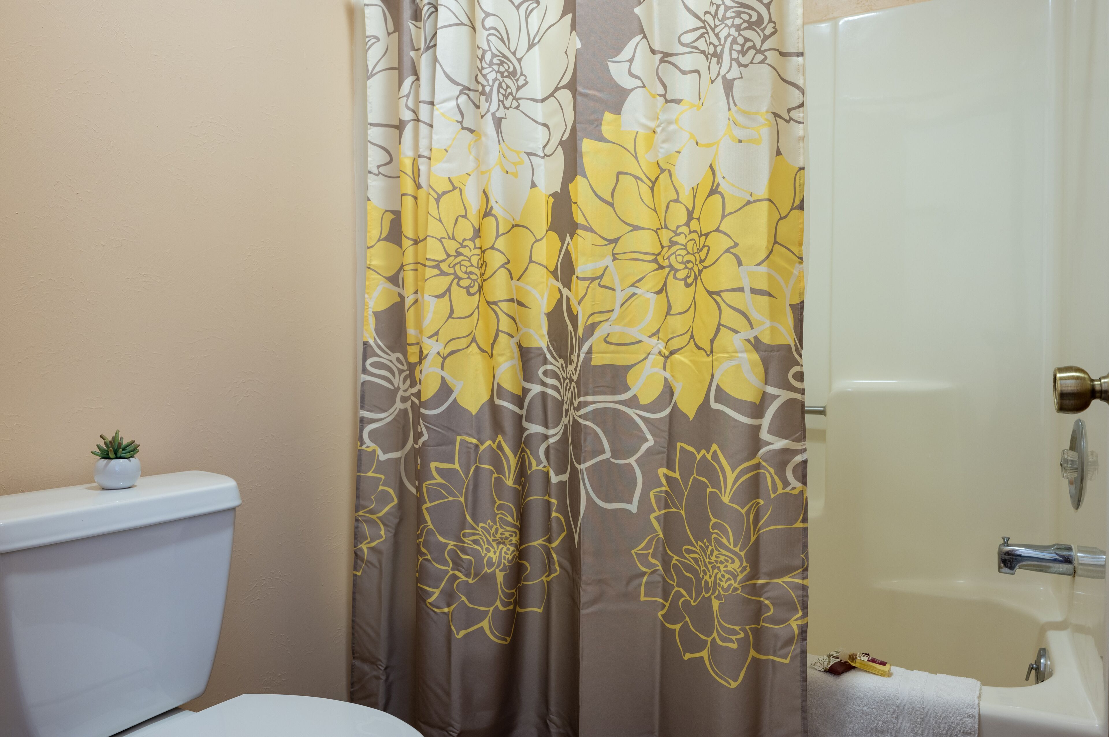 A bathroom with a toilet, a shower curtain with floral patterns, and a bathtub.