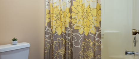 Et badeværelse med toilet, bruseforhæng med blomstermønster og badekar.