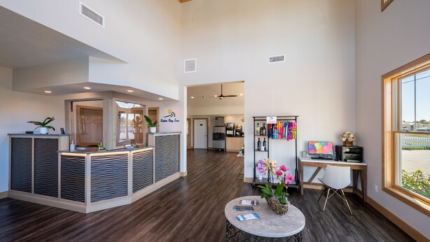 A spacious lobby with a reception desk, a seating area with a round table, and a view of the parking lot through large windows. - Sister Bay Inn (Sister Bay)