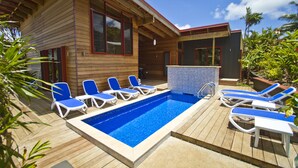 Uma casa de madeira com piscina, cadeiras de descanso azuis e uma banheira de hidromassagem.