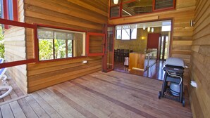 Interior de uma cabana de madeira com área de jantar, churrasqueira e porta de vidro deslizante que dá para uma varanda.