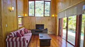 Uma sala de estar espaçosa com uma televisão grande, piso de madeira e uma porta de vidro deslizante para um deck.