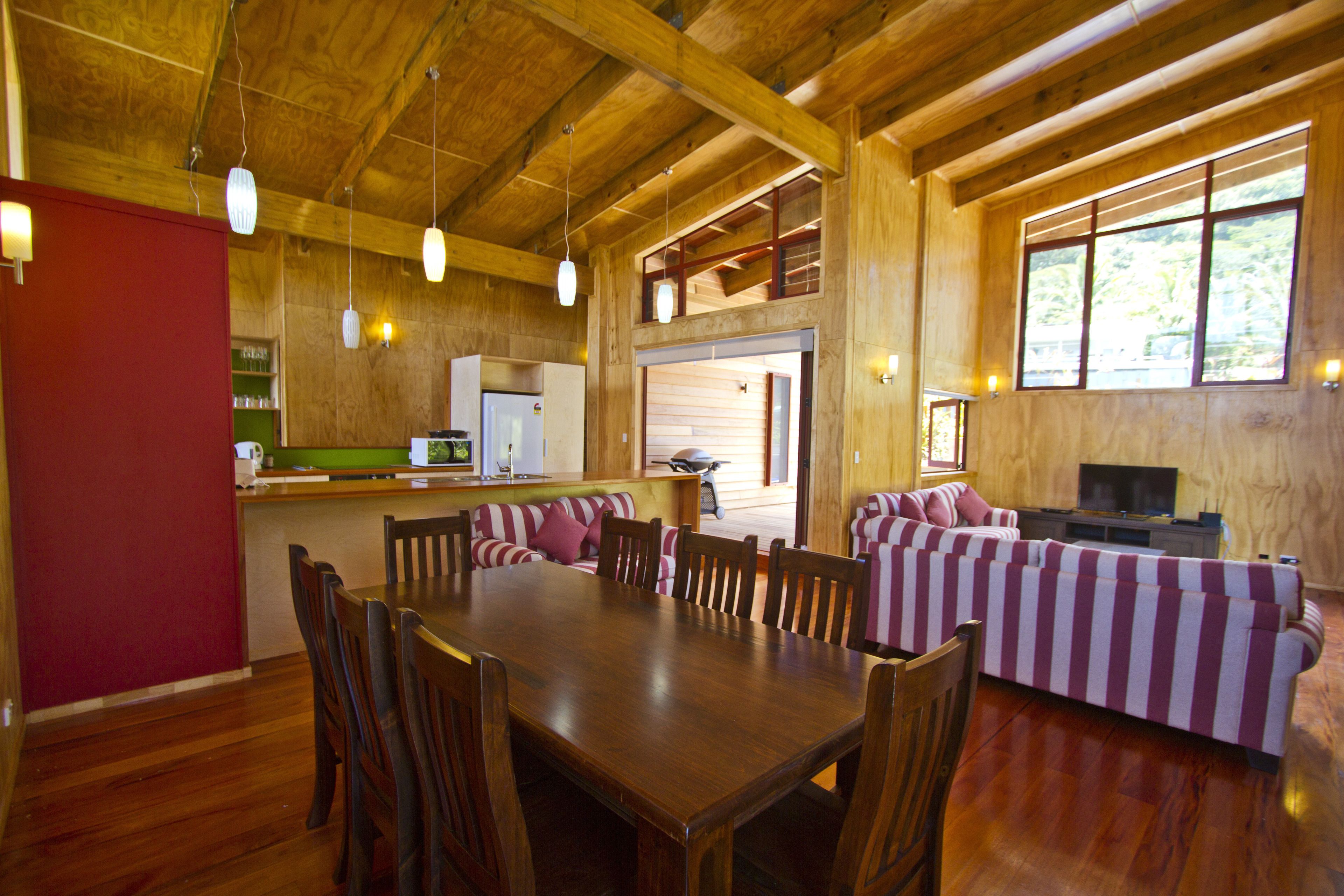 A wooden interior with a dining table, chairs, a sofa, and a television.