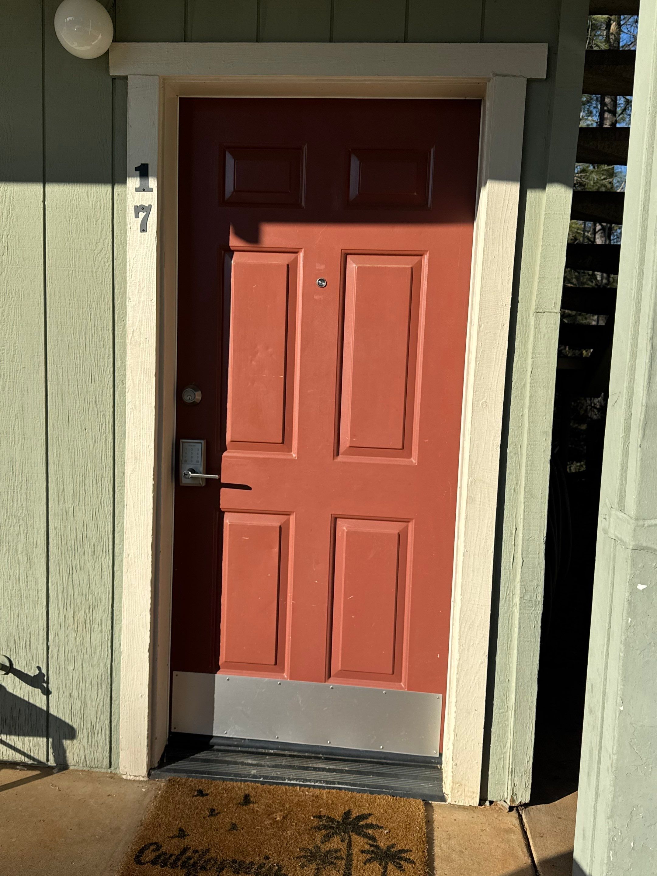A red door with a mailbox and a doormat with palm tree designs.