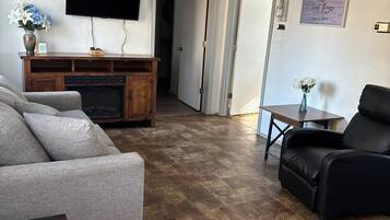 Una sala de estar con un sofá gris, un sillón de cuero negro, un mueble de madera para entretenimiento y un televisor de pantalla plana montado en la pared.