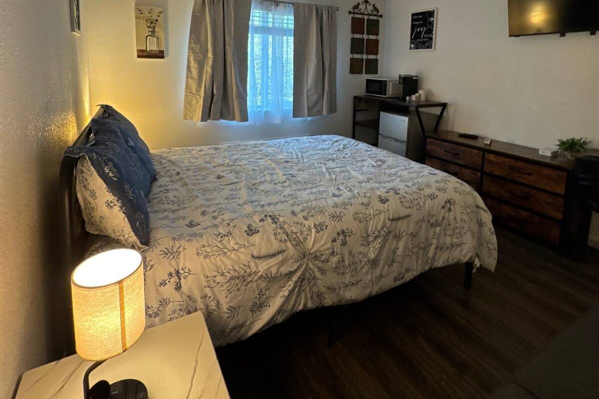 Een slaapkamer met een bed, een bureau, een stoel, een lamp en een televisie.