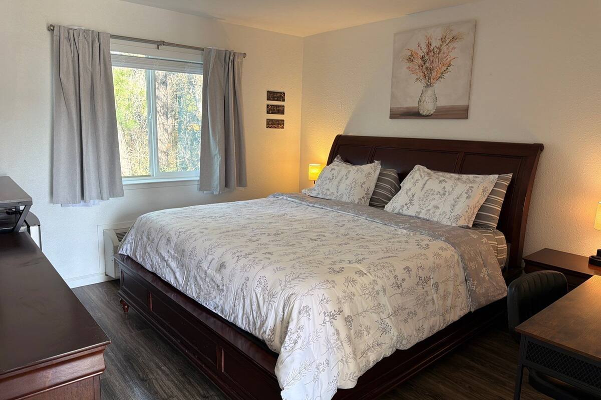 Een slaapkamer met een groot bed, een bureau, een stoel, een raam met gordijnen en een wandlamp.
