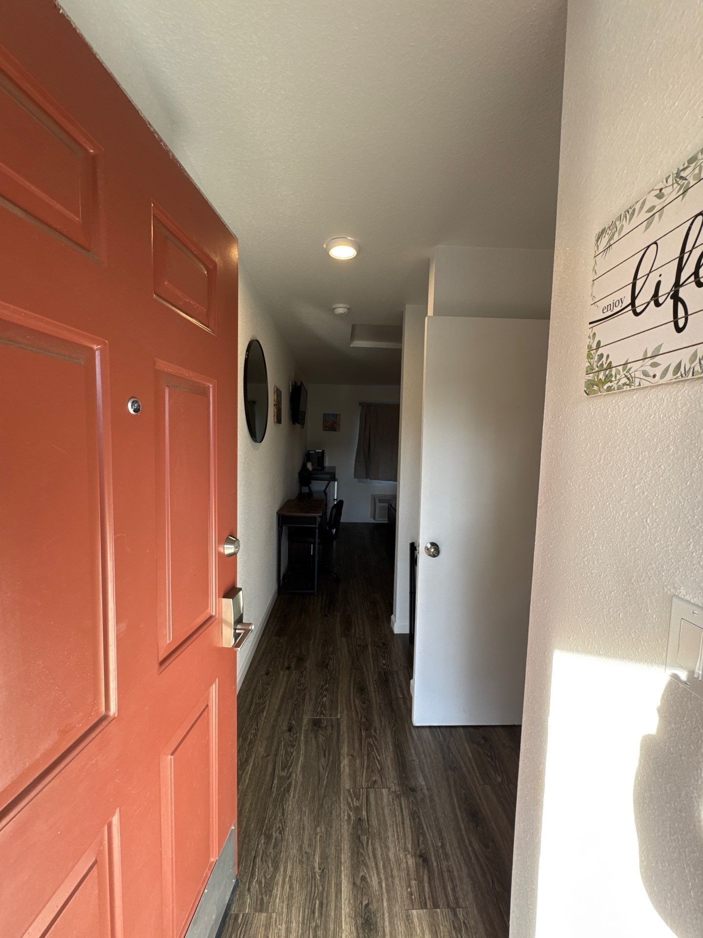 A hallway with a red door, a white door, and a kitchen area in the background.