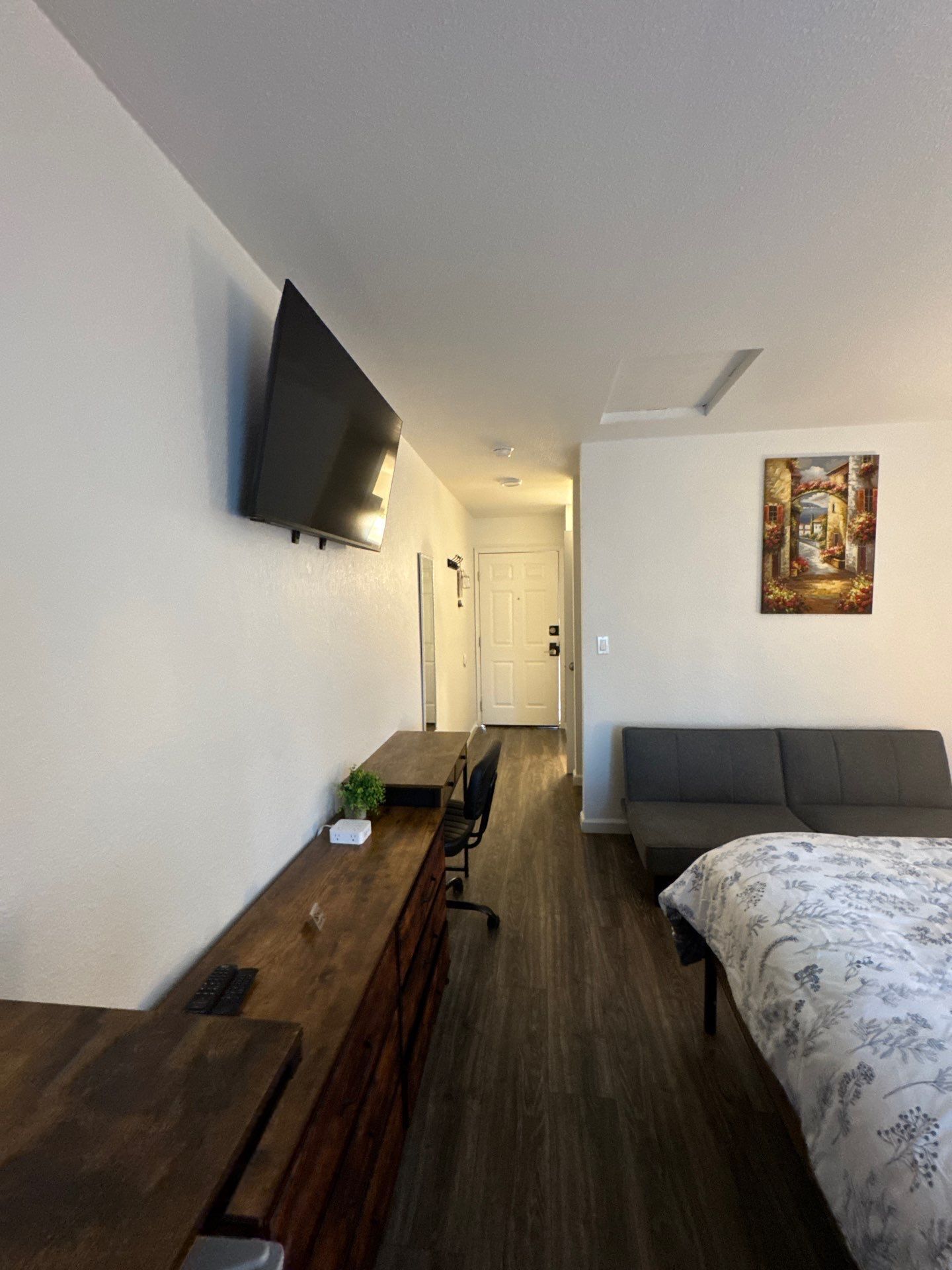 Ein Hotelzimmer mit einem Holztisch, einem Flachbildfernseher an der Wand, einem grauen Sofa und einem Gemälde.